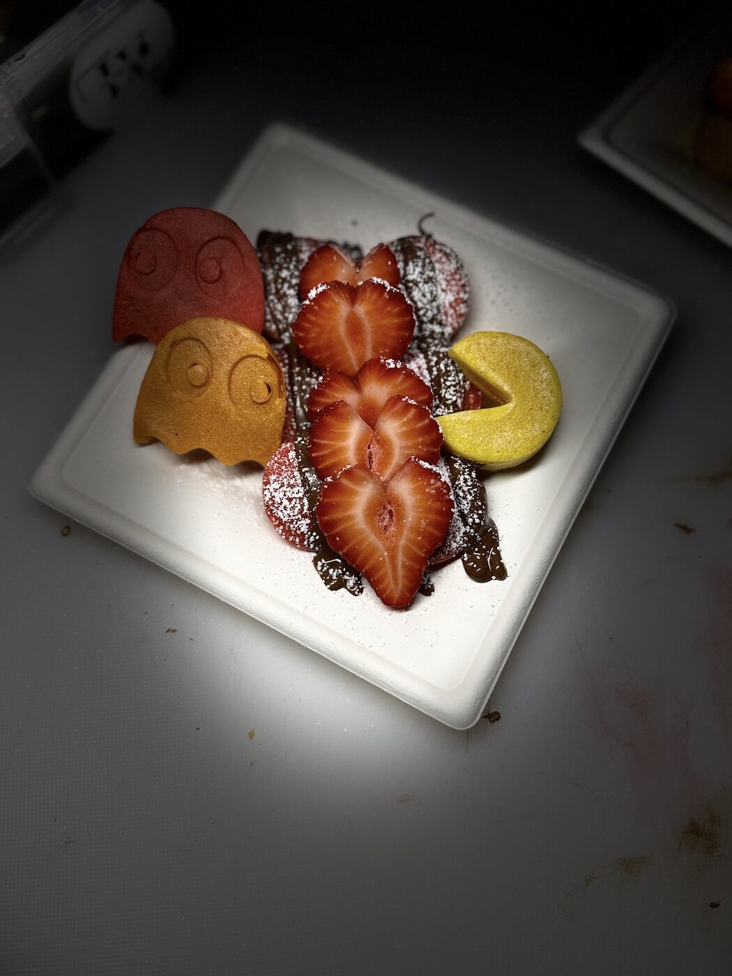 Mini pancakes shaped as arcade characters with strawberries and powdered sugar